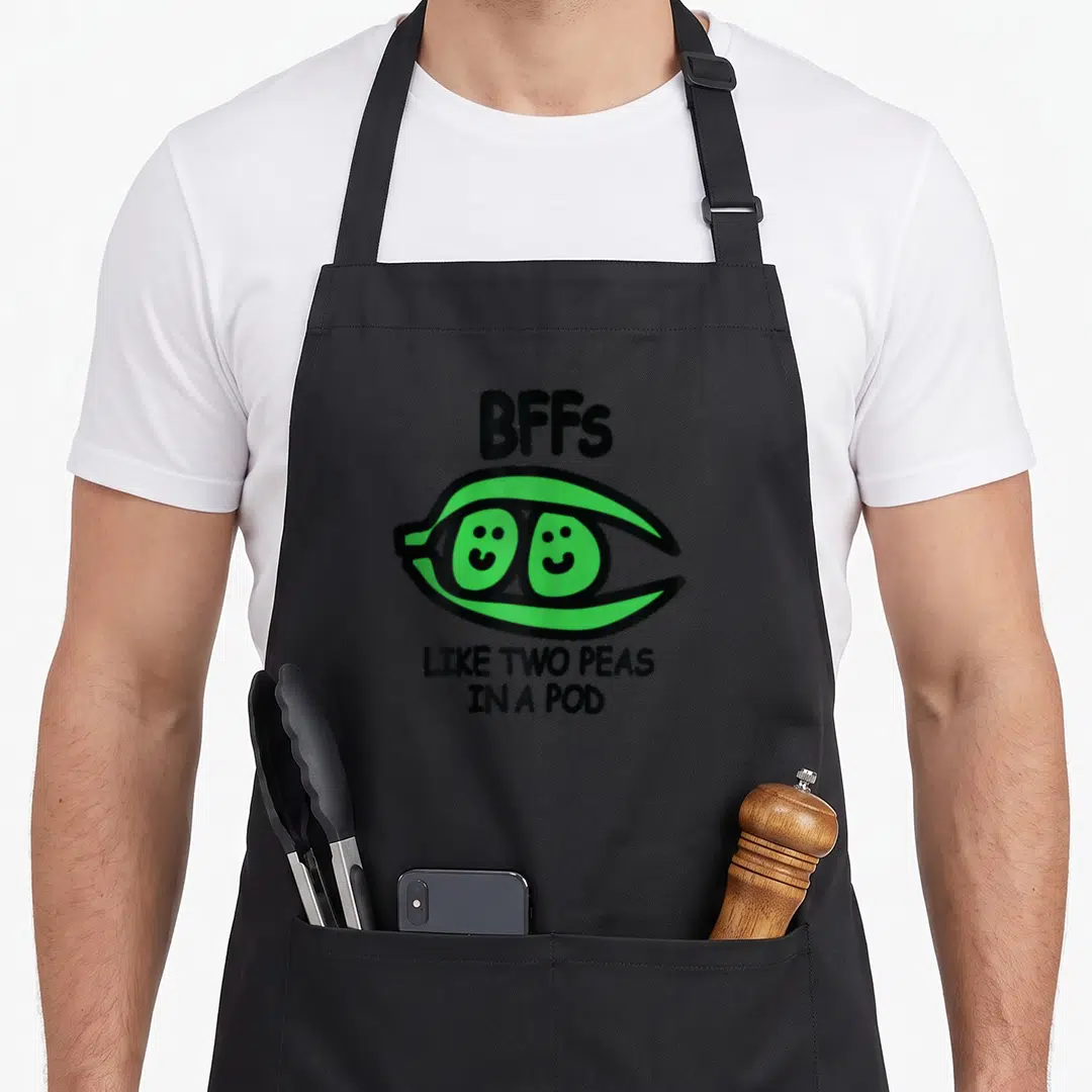 Bff pod aprons - Green pea pod with two smiling peas and BFFs text in black — shown on a black cotton canvas apron against a white background