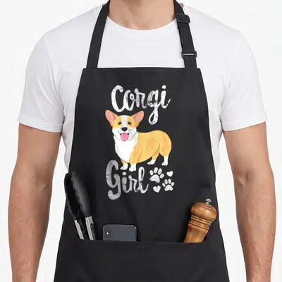Corgi puppy dog apron - Cartoon corgi in white and orange with Corgi Girl text and paw prints — shown on a black cotton canvas apron against a white background