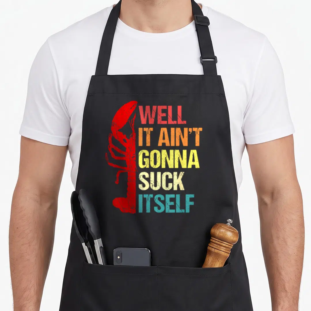 Well cajun aprons - Red lobster silhouette beside stacked multi-colored text reading Well It Ain't Gonna Suck Itself — shown on a black cotton canvas apron against a white background