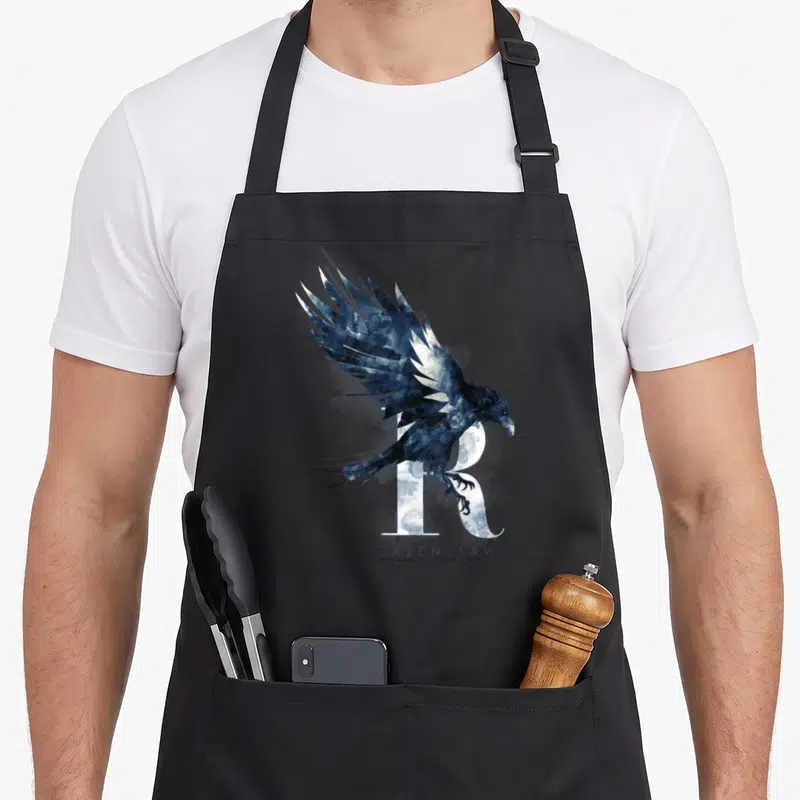 Watercolor ravenclaw apron - Blue watercolor raven perched on white letter R with RAVENCLAW text below — shown on a black cotton canvas apron against a white background
