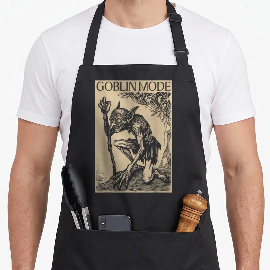 Goblin medieval apron - GOBLIN MODE text above a goblin holding a staff in greyish-brown line art on beige — shown on a black cotton canvas apron against a white background