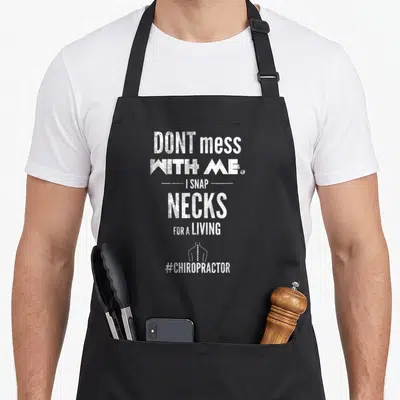 Chiropractor snap aprons - White distressed text reading I SNAP NECKS FOR A LIVING above a small spine graphic — shown on a black cotton canvas apron against a white background