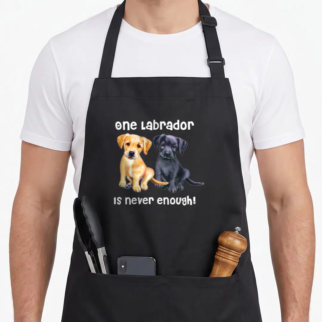 Pet labrador apron - Realistic yellow and black puppies with one Labrador IS never enough text — shown on a black cotton canvas apron against a white background