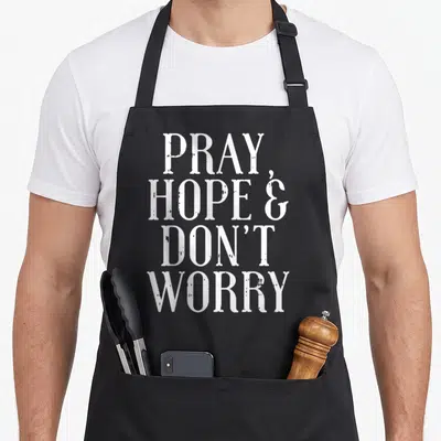 Hope catholic apron - White stacked text reading PRAY HOPE AND DON'T WORRY — shown on a black cotton canvas apron against a white background