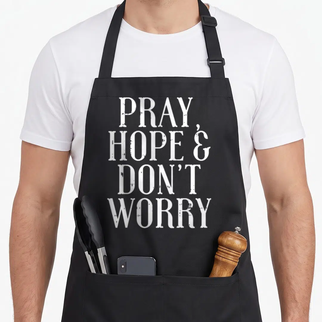 Hope catholic apron - White stacked text reading PRAY HOPE AND DON'T WORRY — shown on a black cotton canvas apron against a white background
