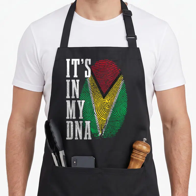 Guyanese pride apron - Vertical IT'S IN MY DNA text beside green yellow red fingerprint with distressed texture — shown on a black cotton canvas apron against a white background
