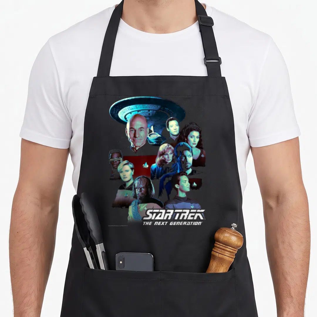 Generation crew apron - Star Trek Next Generation cast collage below spaceship with blue white red uniforms — shown on a black cotton canvas apron against a white background