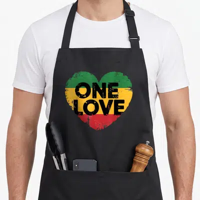 Rastafarian reggae apron - Heart with green yellow red stripes and black one love text — shown on a black cotton canvas apron against a white background