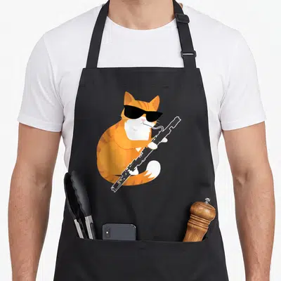 Musical cat apron - Orange tabby cat wearing black sunglasses playing a black clarinet in cartoon style — shown on a black cotton canvas apron against a white background