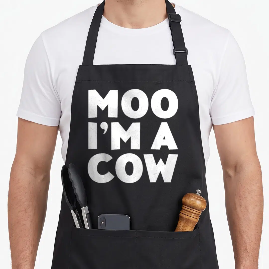 Moo cow apron - White stacked text reading MOO I'M A COW on dark background — shown on a black cotton canvas apron against a white background