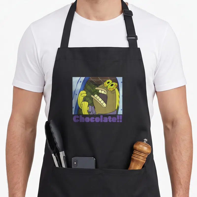 Scream fish apron - Yellow fish character screaming inside rectangular frame with net background and purple Chocolate!! — shown on a black cotton canvas apron against a white background