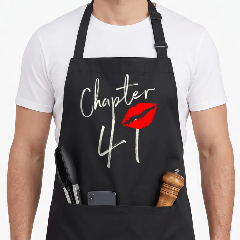 Chapter est birthday apron - White brush script Chapter 41 text next to a pair of red lips — shown on a black cotton canvas apron against a white background