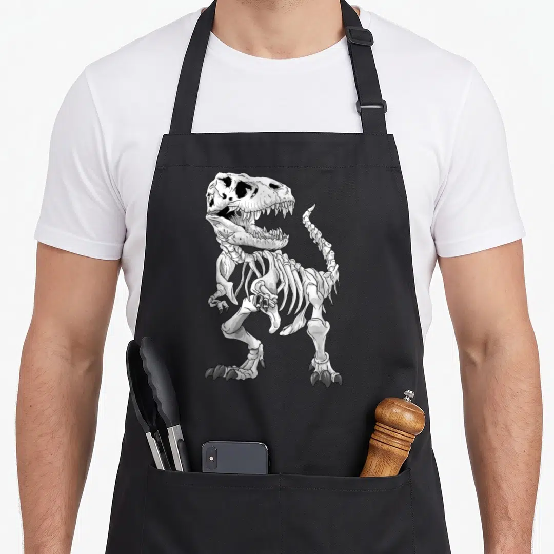 Rex skeleton apron - White and grey line art of a standing T-Rex skeleton with sharp claws on a grey background — shown on a black cotton canvas apron against a white background