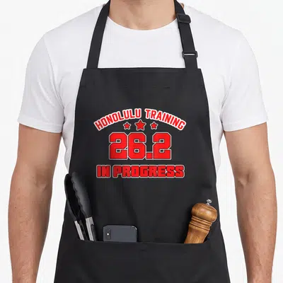 Honolulu training apron - Red text HONOLULU TRAINING 26.2 IN PROGRESS with three stars — shown on a black cotton canvas apron against a white background