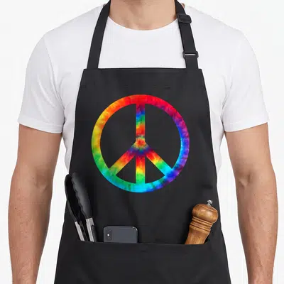 Hippy tie-dye apron - Rainbow tie-dye peace symbol graphic on black fabric — shown on a black cotton canvas apron against a white background