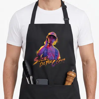 Dustin stranger apron - Photo of person with cap and radio, yellow purple pink blue text reading Suzie Do You Copy — shown on a black cotton canvas apron against a white background