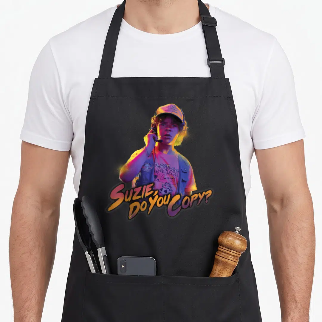 Dustin stranger apron - Photo of person with cap and radio, yellow purple pink blue text reading Suzie Do You Copy — shown on a black cotton canvas apron against a white background