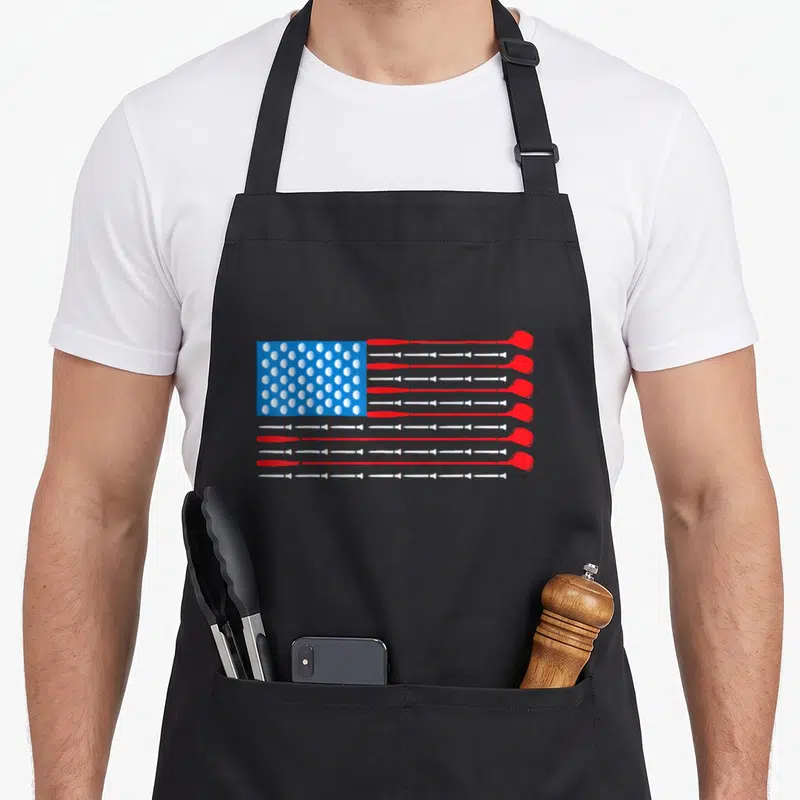 Patriotic golf apron - USA flag pattern made of red and white golf clubs and white golf balls on blue background — shown on a black cotton canvas apron against a white background