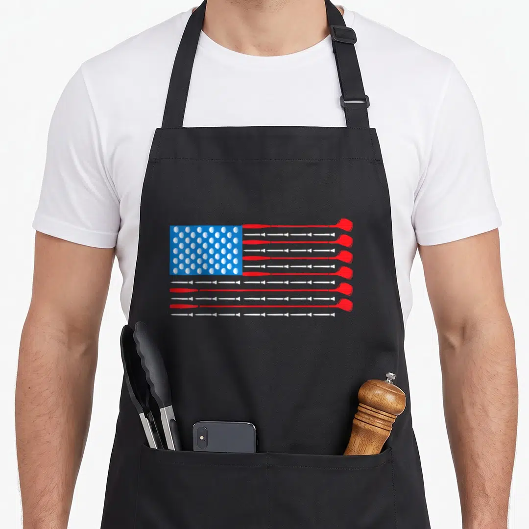 Patriotic golf apron - USA flag pattern made of red and white golf clubs and white golf balls on blue background — shown on a black cotton canvas apron against a white background