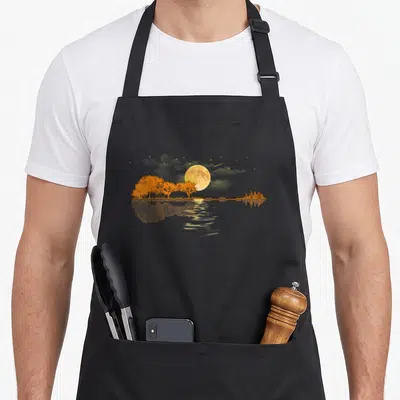 Moonlight musician apron - Realistic yellow moon, orange trees, city skyline, and shooting star reflected in water — shown on a black cotton canvas apron against a white background