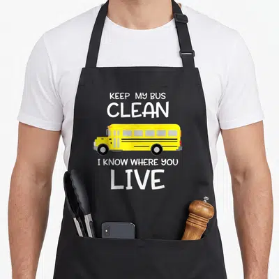 Appreciation omnibus apron - Yellow school bus with white text keep my bus clean i know where you live — shown on a black cotton canvas apron against a white background