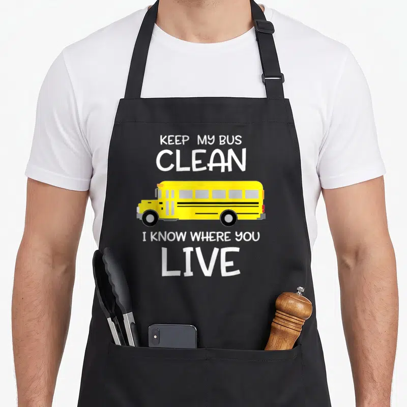 Appreciation omnibus apron - Yellow school bus with white text keep my bus clean i know where you live — shown on a black cotton canvas apron against a white background