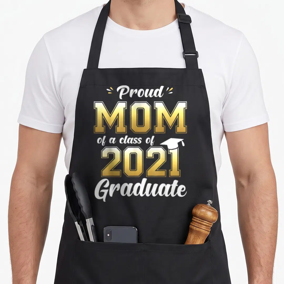 Proud mom class apron - Gold and white text Proud Mom of a class of 2021 Graduate with cap icon — shown on a black cotton canvas apron against a white background