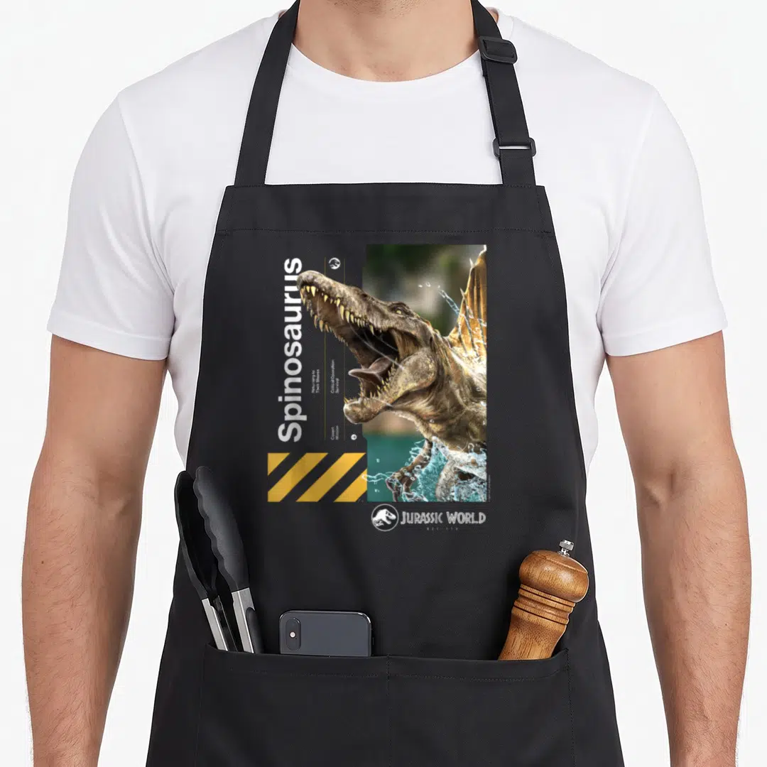 Jurassic spinosaurus apron - Brown spino head with vertical white text and yellow diagonal stripes — shown on a black cotton canvas apron against a white background