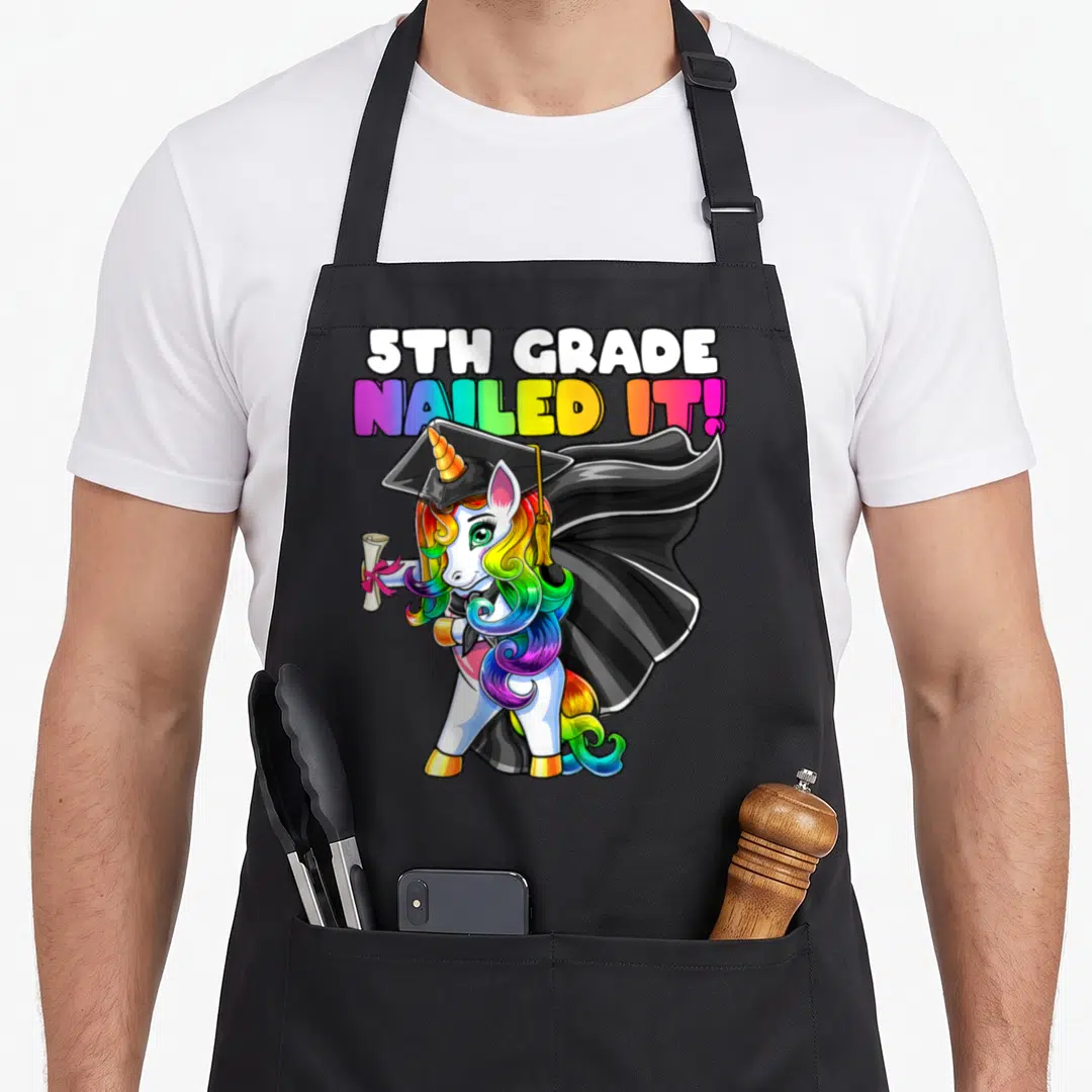 Flossing 5th unicorn apron - Cartoon unicorn in cap and gown holding diploma under 5th Grade Nailed It text — shown on a black cotton canvas apron against a white background