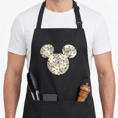 Floral daisy apron - Mickey Mouse head silhouette filled with white and yellow daisy flowers — shown on a black cotton canvas apron against a white background
