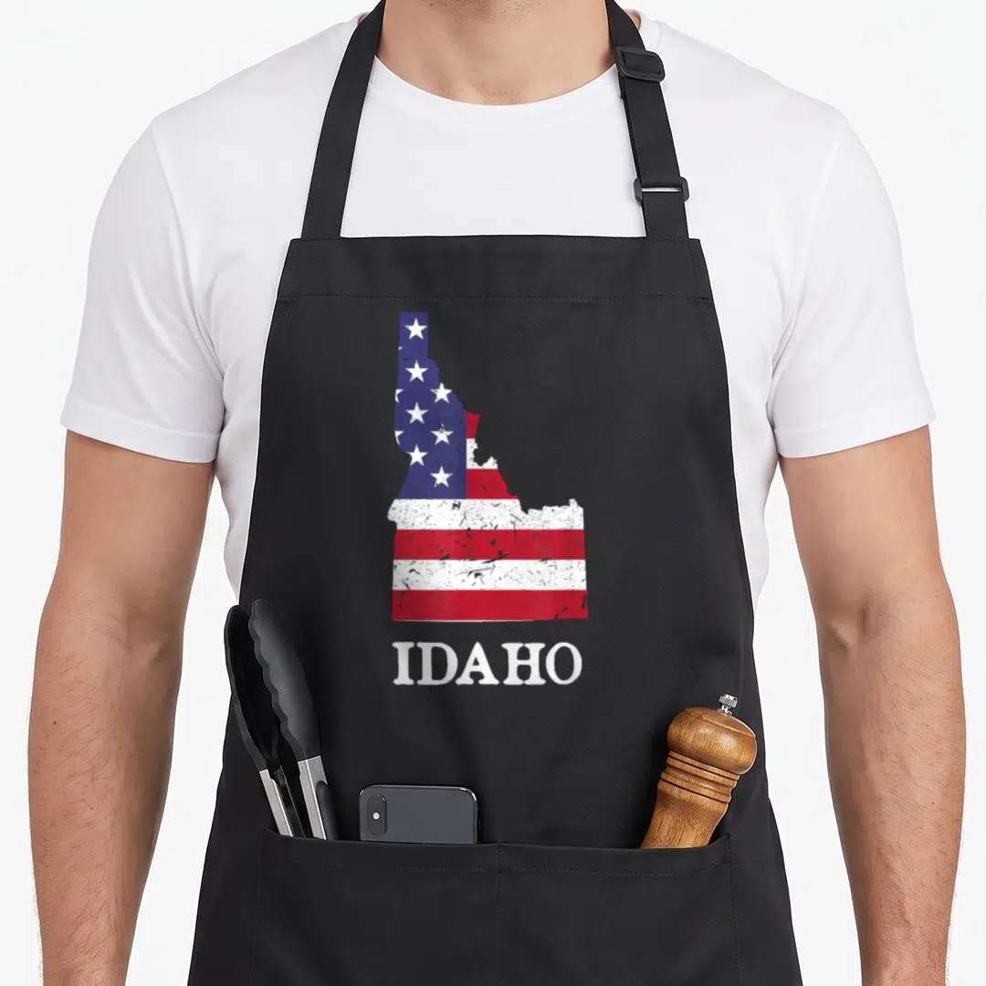Idaho 4th of july apron - Distressed Idaho state map filled with red white blue flag pattern and white IDAHO text below — shown on a black cotton canvas apron against a white background