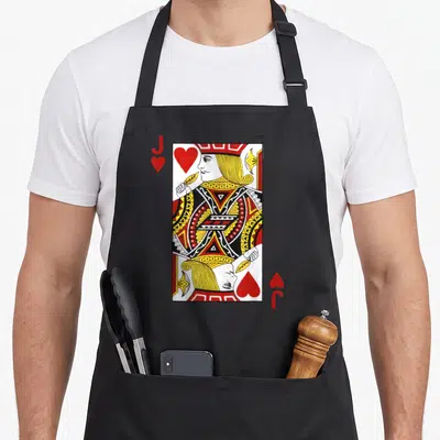 Blackjack jack apron - Red and yellow jack of hearts playing card illustration on black fabric — shown on a black cotton canvas apron against a white background