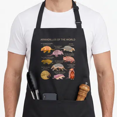 Specy armadillo apron - Ten cartoon armadillos with scientific names and pink orange grey brown shells — shown on a black cotton canvas apron against a white background