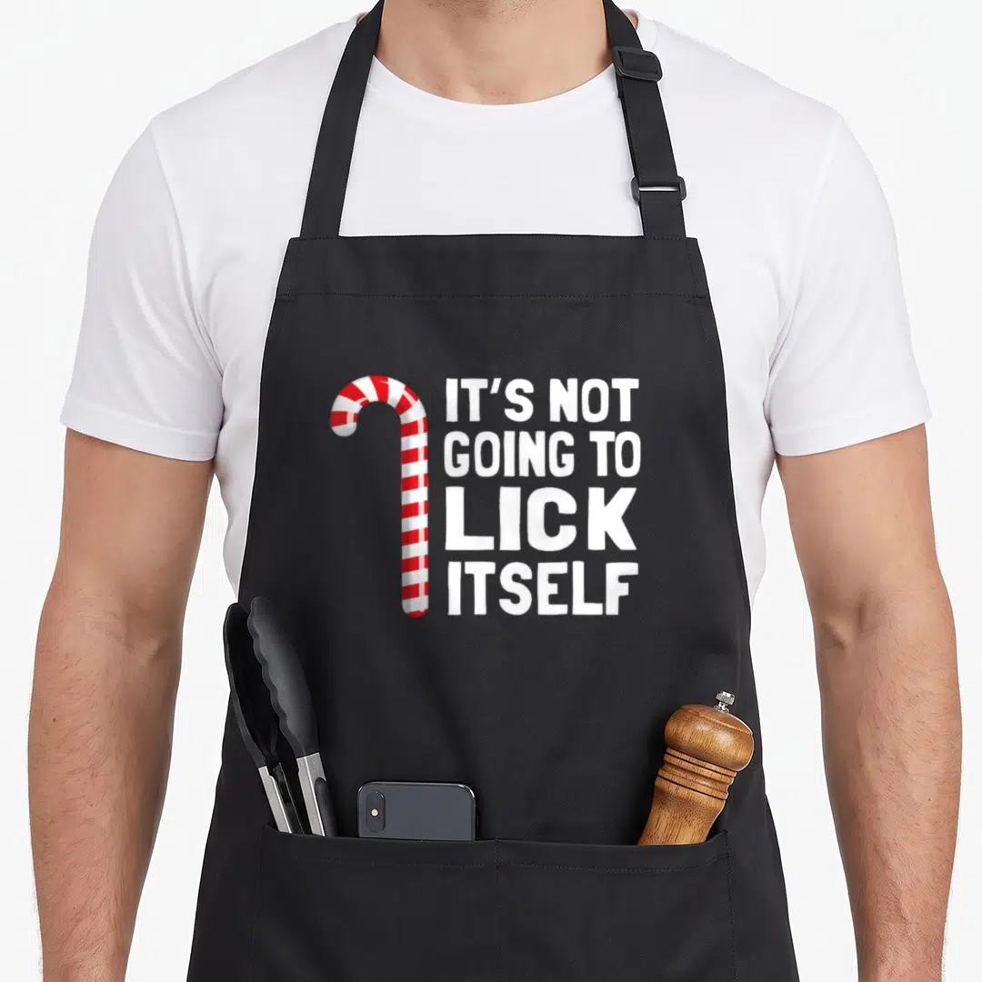 Lick candy cane apron - Red and white striped candy cane next to four lines of white text reading IT'S NOT GOING — shown on a black cotton canvas apron against a white background