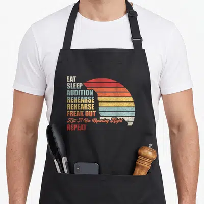 Geek theater apron - Stacked text EAT SLEEP AUDITION REHEARSE REHEARSE FREAK OUT Kill It On Opening Night REPEAT — shown on a black cotton canvas apron against a white background