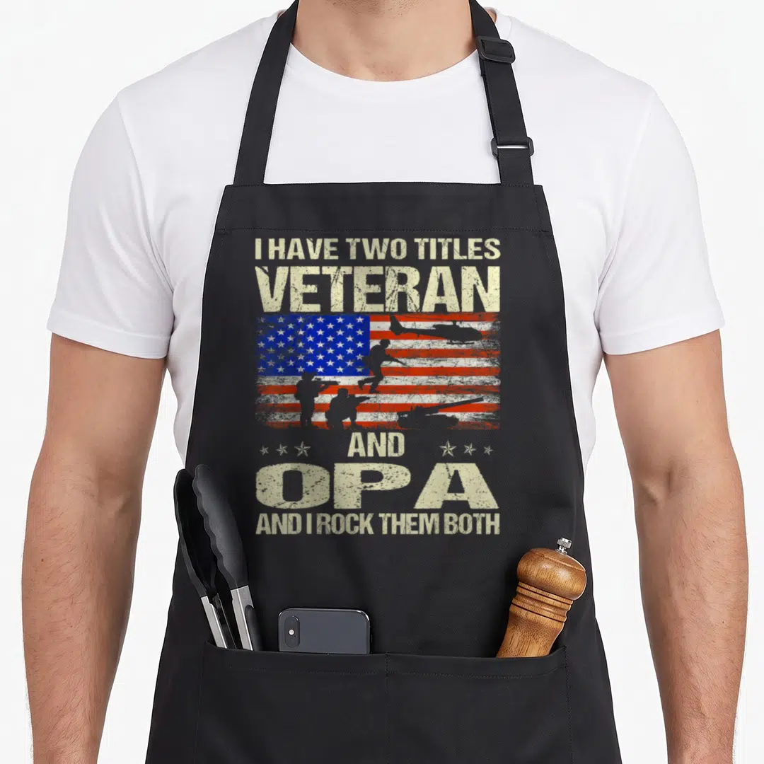 Title veteran grandpa apron - Distressed USA flag with soldier silhouettes and text I HAVE TWO TITLES VETERAN AND OPA — shown on a black cotton canvas apron against a white background