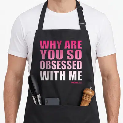 Obsessed mean girls apron - Stacked pink to white gradient text reading WHY ARE YOU SO OBSESSED WITH ME — shown on a black cotton canvas apron against a white background