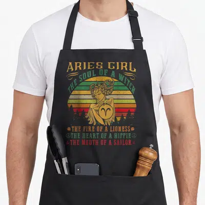 Soul aries kitchen apron - Retro woman holding Aries symbol with stacked text Soul of a Witch Mouth of a Sailor — shown on a black cotton canvas apron against a white background
