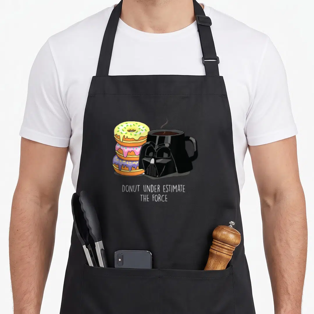 Coffee donut apron - Three stacked donuts next to Darth Vader mug with pun text below — shown on a black cotton canvas apron against a white background