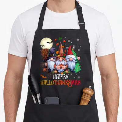 Hallothanksmas merry christmas apron - Three gnomes holding broom and pumpkin under moon with bats and tree, stacked — shown on a black cotton canvas apron against a white background