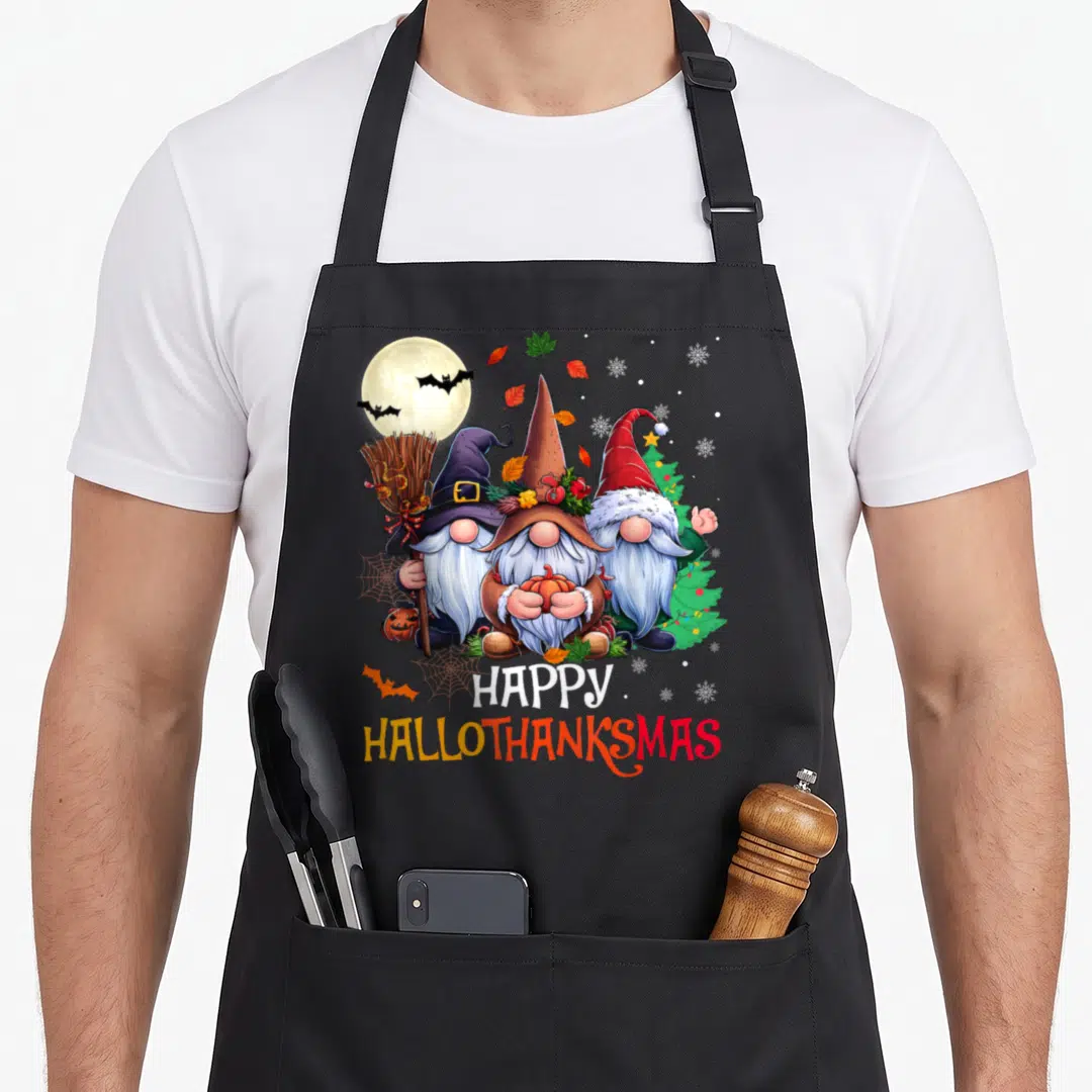 Hallothanksmas merry christmas apron - Three gnomes holding broom and pumpkin under moon with bats and tree, stacked — shown on a black cotton canvas apron against a white background