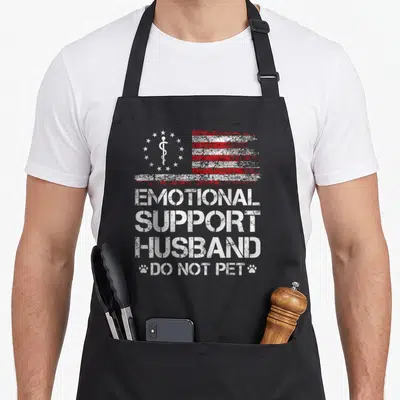 Emotional american flag apron - Distressed red white flag with caduceus and text EMOTIONAL SUPPORT HUSBAND DO NOT PET — shown on a black cotton canvas apron against a white background