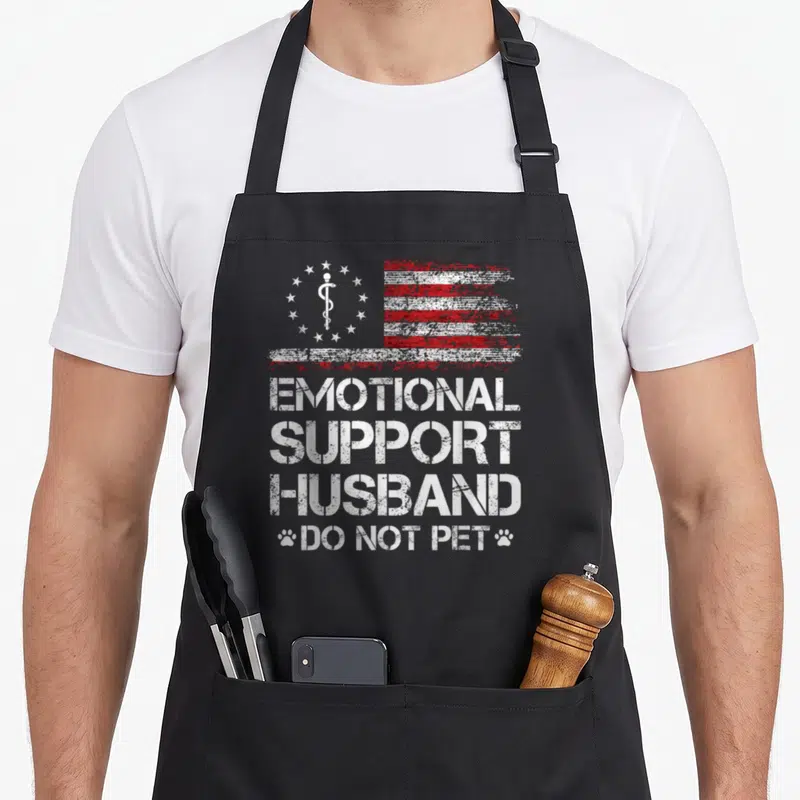 Emotional american flag apron - Distressed red white flag with caduceus and text EMOTIONAL SUPPORT HUSBAND DO NOT PET — shown on a black cotton canvas apron against a white background