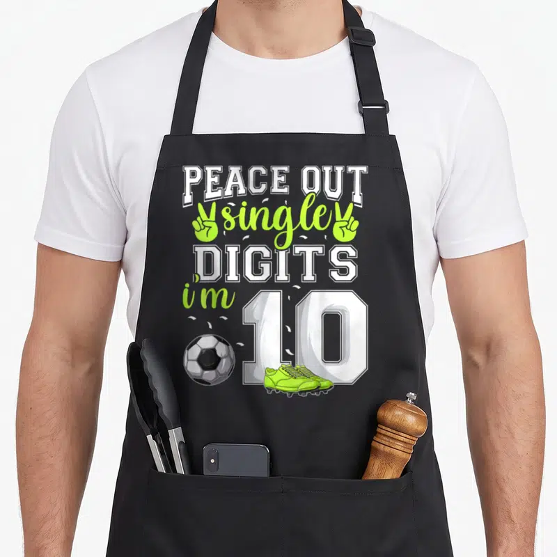 Single birthday apron - PEACE OUT single DIGITS i'm 10 text with soccer ball and lime cleats — shown on a black cotton canvas apron against a white background