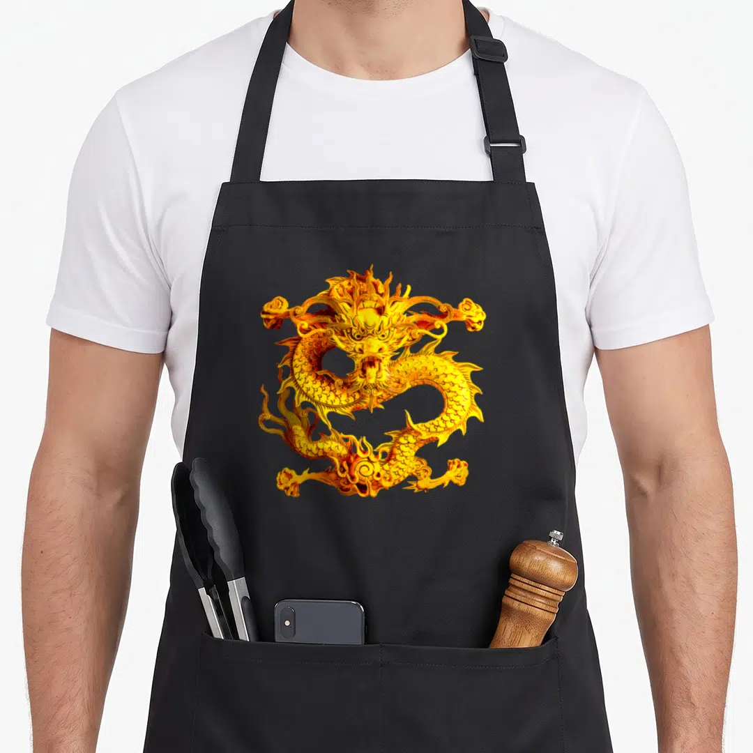 Fearless golden apron - Centered golden and yellow dragon illustration on black background — shown on a black cotton canvas apron against a white background