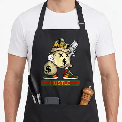 Stack money apron - Cartoon money bag with X eyes holding gun and cash, HUSTLE text in red green bar — shown on a black cotton canvas apron against a white background