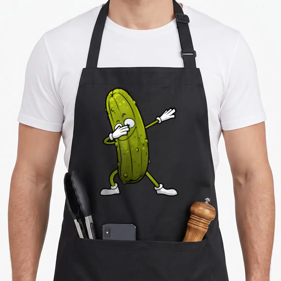 Keto pickle apron - Cartoon green pickle character dabbing with white gloves and shoes — shown on a black cotton canvas apron against a white background