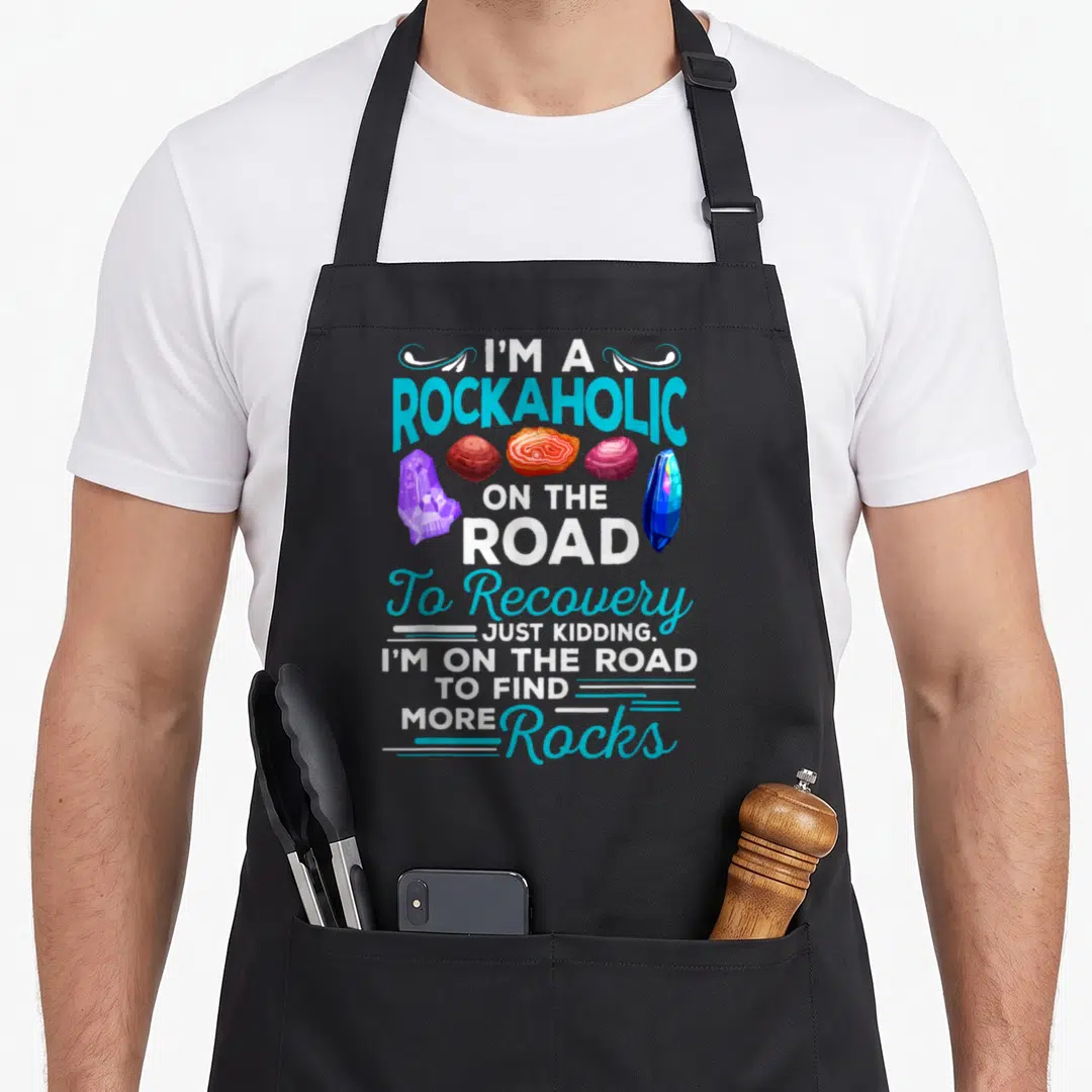 Rockaholic colorful aprons - I'M A ROCKAHOLIC text with five colorful rocks and crystals stacked vertically — shown on a black cotton canvas apron against a white background