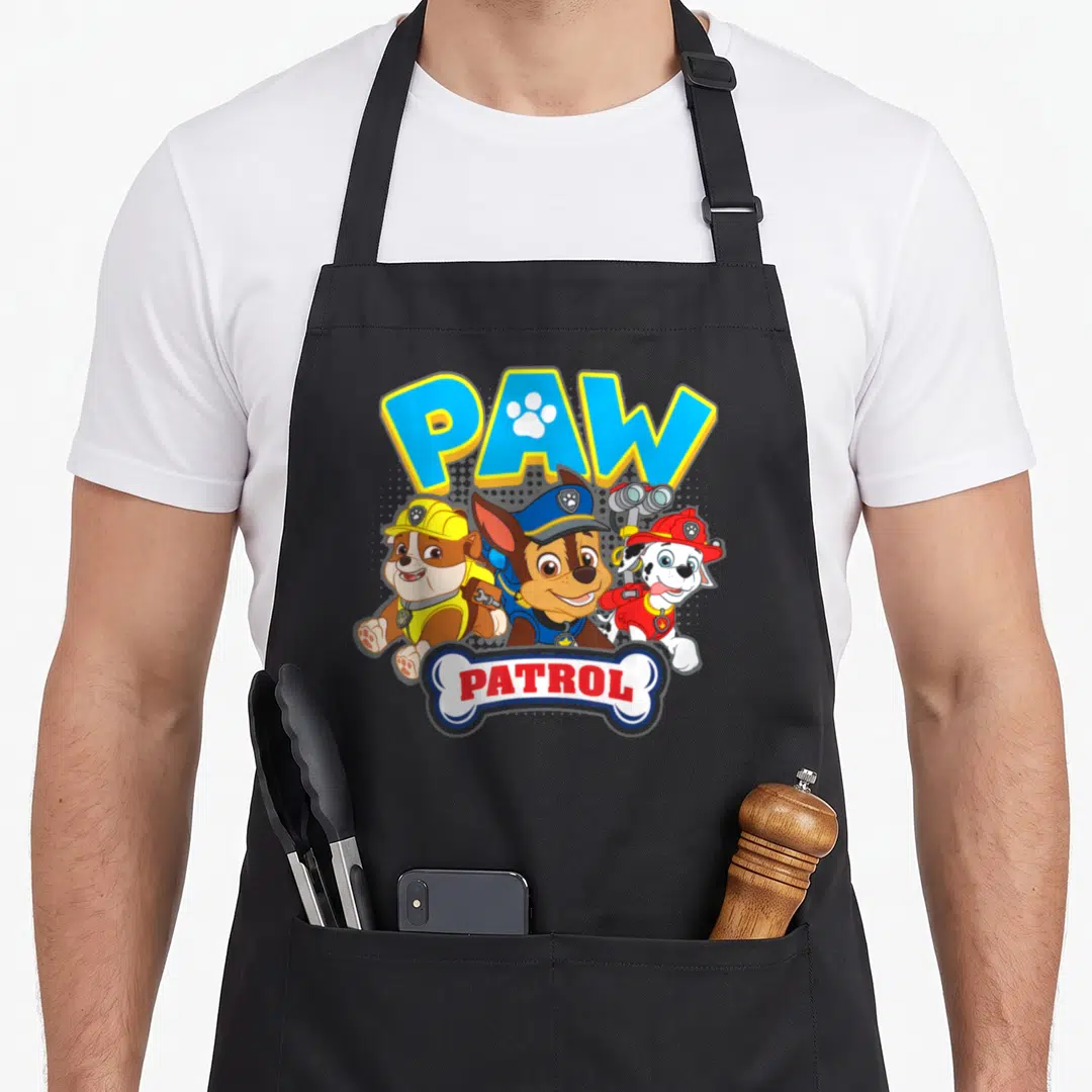 Chase marshalls apron - PAW PATROL text above three cartoon puppies and PATROL inside a bone shape below — shown on a black cotton canvas apron against a white background