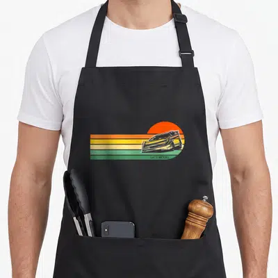 Sunset track apron - Retro race car on orange sun with horizontal stripes and LATE MODEL text — shown on a black cotton canvas apron against a white background